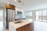 Located at 301 M St SW in Washington, DC, this thoughtfully designed two-bedroom, two-bathroom residence offers a clean, contemporary aesthetic throughout. Light wood-tone flooring flows seamlessly across the open-concept living space, complementing the neutral color palette and creating a warm, cohesive ambiance.

The kitchen is a standout feature, showcasing a large waterfall-edge island with an integrated sink, rich walnut-toned lower cabinetry, glossy white upper cabinets, and a full suite of stainless steel appliances including a built-in oven, cooktop, microwave, and refrigerator. The kitchen opens directly to the combined dining and living area, which benefits from abundant natural light and direct access to a private balcony with open city views.

Both bedrooms are well-proportioned and bright, with large windows framing views of the Washington, DC skyline. The primary bedroom is served by an en-suite bathroom featuring marble-look tile, a glass-enclosed shower, and a walnut-finished vanity. The second bathroom offers a soaking tub with full marble-tile surround. Four closets provide generous storage throughout, and a dedicated in-unit laundry area adds everyday convenience. Exposed concrete architectural columns lend an urban, industrial accent to the otherwise refined interior.