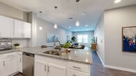 Located at 3014 Bicentennial Dr in Jacksonville, FL, this single-story residence offers a thoughtfully designed open-concept floor plan with contemporary finishes throughout. The kitchen serves as a central hub of the home, featuring granite countertops, white shaker-style cabinetry, a subway tile backsplash, stainless steel appliances, and a large peninsula with an undermount sink and pendant lighting overhead. Wood-style flooring extends through the main living areas, creating a cohesive visual flow from the kitchen through the dining area and into the living room.

The dining area comfortably accommodates a full-sized table and connects naturally to the living room, which benefits from a large window and exterior door that allow generous natural light to fill the space. The bedrooms are carpeted for comfort, each offering ceiling fans, natural light through sizable windows, and a calm, neutral color palette. The bathroom is well-appointed with a granite-topped double vanity, white cabinetry, wood-style flooring, and a tiled soaking tub and shower combination. Soft gray tones used throughout the home contribute to a clean, modern, and welcoming ambiance.