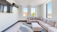 Located at 116 E Randolph Ave in Enid, Oklahoma, this modern one-bedroom, one-bathroom unit offers a well-designed layout across a single floor. The space features a contemporary aesthetic throughout, with clean white walls, neutral flooring, and bold navy baseboards that add a distinctive design touch.

The kitchen is a standout feature, equipped with grey shaker-style cabinetry, a full suite of stainless steel appliances including a refrigerator, dishwasher, microwave, and range, as well as a sleek white quartz waterfall island with seating for multiple bar stools. Striking black dome pendant lights illuminate the workspace, creating a polished, modern atmosphere.

The living room is bright and inviting, with two large windows that frame views of the surrounding Enid cityscape and mature trees, filling the room with natural light. A wall-mounted TV and ample space for seating make it a functional and comfortable gathering area.

The generously sized bedroom features elevated ceilings, a ceiling fan, wall-mounted TV, and a built-in closet with paneled grey doors. Large windows offer additional city views and natural light. The bathroom is clean and functional, finished with a sliding glass walk-in shower, vanity, and neutral tile flooring.