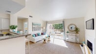This thoughtfully designed single-floor residence offers a cohesive coastal-inspired aesthetic throughout its well-appointed spaces. The open-concept living room is a welcoming centerpiece, featuring plush carpeting, vaulted ceilings, and abundant natural light streaming in through large sliding glass doors that lead directly to a private outdoor patio overlooking lush greenery. A fireplace with a clean white surround adds warmth and character to the living area, complemented by an adjacent dining nook with a glass-top table and sheer curtains framing a sunlit window. The kitchen is efficiently laid out with white cabinetry, granite-style countertops, stainless steel appliances, and a breakfast bar that connects seamlessly to the living space. Both bedrooms are generously sized, carpeted for comfort, and filled with natural light through large windows dressed with soft curtains and blinds. The full bathroom is clean and functional, offering a tiled tub-shower combination, granite-topped vanity, and ample storage via a built-in closet. Throughout the residence, a warm, neutral color palette and consistent design language create a calm, relaxed ambiance ideal for comfortable everyday living.