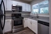 Located at 3399 Lakebrook Blvd in Knoxville, Tennessee, this single-floor residence offers a thoughtfully designed layout with a cohesive blend of comfort and functionality. The kitchen is a standout feature, outfitted with white cabinetry, granite countertops, and a full suite of stainless steel appliances including a refrigerator, range with microwave above, and a sink with a window overlooking the outdoors. Wood-style flooring grounds the kitchen, which connects to the living area via a pass-through counter. The open living area is carpeted and bright, with natural light filtering in and a clear sightline to the kitchen. A dedicated bedroom features sliding glass doors that open to a private outdoor balcony or patio, inviting in natural light and outdoor views. Additional bedrooms are carpeted, quiet, and well-lit by multiple windows with blinds. The bathroom is clean and functional, featuring a granite-top vanity with white cabinetry, a framed mirror, stylish sconce lighting, and a tub-shower combination with wood-style flooring. Throughout the space, neutral tones and consistent finishes create a calm, cohesive atmosphere suited for everyday living.
