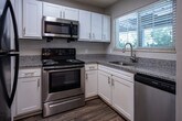 Located at 3399 Lakebrook Blvd in Knoxville, Tennessee, this single-floor residence offers a thoughtfully designed layout with a cohesive blend of comfort and functionality. The kitchen is a standout feature, outfitted with white cabinetry, granite countertops, and a full suite of stainless steel appliances including a refrigerator, range with microwave above, and a sink with a window overlooking the outdoors. Wood-style flooring grounds the kitchen, which connects to the living area via a pass-through counter. The open living area is carpeted and bright, with natural light filtering in and a clear sightline to the kitchen. A dedicated bedroom features sliding glass doors that open to a private outdoor balcony or patio, inviting in natural light and outdoor views. Additional bedrooms are carpeted, quiet, and well-lit by multiple windows with blinds. The bathroom is clean and functional, featuring a granite-top vanity with white cabinetry, a framed mirror, stylish sconce lighting, and a tub-shower combination with wood-style flooring. Throughout the space, neutral tones and consistent finishes create a calm, cohesive atmosphere suited for everyday living.