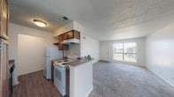 Located at 9100 Andrews in Odessa, Texas, this single-story unit offers a practical and well-organized layout designed for comfortable everyday living. The open-concept kitchen flows directly into the living area, creating a connected and functional space. The kitchen is equipped with warm-toned wood cabinetry, a electric range, refrigerator, and a peninsula with a laminate countertop that doubles as a casual dining or prep space. Wood-look flooring runs throughout the kitchen, providing a durable and easy-to-maintain surface. The living area is generously sized, featuring plush carpeting, a textured ceiling, and a large front-facing window with vertical blinds that invites abundant natural light while offering views of the surrounding exterior. The front entry door is positioned adjacent to this window, providing a welcoming focal point to the space. The bedroom is carpeted and includes a ceiling fan, a window for additional ventilation and light, and direct access to a closet and bathroom. The bathroom is well-appointed with a single-sink vanity featuring wood cabinetry and a laminate countertop, a full tub-shower combination with tiled surround, and wood-look flooring. Throughout the unit, the neutral color palette and consistent finishes create a cohesive and move-in-ready environment.