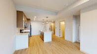 This contemporary single-floor residence showcases a thoughtfully designed open-concept layout with clean lines and modern finishes. The kitchen serves as the heart of the space, featuring warm-toned cabinetry, a classic white subway tile backsplash, stainless steel appliances including a refrigerator, range, and microwave, and a white quartz island with an integrated sink and a stylish industrial-cage pendant light overhead. Light hardwood-style flooring flows throughout, lending warmth and visual continuity to each area. The living area benefits from floor-to-ceiling sliding glass doors that invite abundant natural light and provide direct access to an outdoor deck with views of the surrounding cityscape. Additional bedrooms are generously sized, with large black-framed windows—including a striking bank of grid-pane windows—that frame expansive urban views and are complemented by ceiling fans for comfort. A dedicated laundry area houses a stacked GE washer and dryer with built-in shelving for added storage convenience. The bathroom is finished with light wood cabinetry, a white countertop vanity, an undermount sink, a large mirror, and matte black hardware accents throughout. The overall aesthetic is bright, airy, and cohesive, combining modern urban design with functional living spaces.