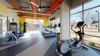 Located at 310 E Springfield Ave in Champaign, IL, this single-floor fitness facility delivers a dynamic and energizing workout environment defined by bold design choices and comprehensive equipment offerings. The space is immediately striking, with high ceilings that expose vivid orange HVAC ductwork and suspended linear lighting, lending an industrial yet vibrant character throughout.

Large floor-to-ceiling windows line the perimeter, flooding the interior with natural light and offering open views of the surrounding streetscape. The flooring transitions between rubberized sport surfaces and striped resilient flooring, clearly delineating zones for different training disciplines.

The strength training area is prominently branded with bold yellow "STRENGTH POWER" lettering on the walls and is outfitted with a full array of selectorized machines. A dedicated functional training zone features an Octagon power rack, kettlebells, battle ropes, a heavy tire, and a punching bag, catering to high-intensity and functional fitness routines. The cardio zone houses a row of treadmills and elliptical machines positioned directly beside the expansive windows, allowing users to train with an energizing view. A separate glassed-in studio space with wood-look flooring provides a clean, versatile area for group classes or individual training. The overall ambiance is motivating, modern, and well-equipped for a wide range of fitness activities.