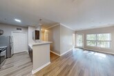 Located at 251 Ridge Lane in Waltham, MA, this well-appointed 2-bedroom, 2-bathroom residence offers a thoughtfully designed single-floor layout. Wood-look flooring and crown molding run throughout the main living areas, lending a clean, cohesive aesthetic. The open-concept kitchen features dark cabinetry, stainless steel appliances, and a peninsula with a white countertop that flows seamlessly into the dining and living areas. Large windows in the living room invite generous natural light and offer pleasant outdoor views of surrounding greenery. A dedicated dining area sits adjacent to the living room, which also includes built-in shelving for added functionality. The hallway connecting the bedrooms is lined with multiple closets — six in total — providing exceptional storage. The spacious primary bedroom includes a ceiling fan, a private en-suite bathroom, and a closet, while the second bedroom is equally bright with its own window and access to natural light. Both bathrooms are finished with wood-look flooring, modern vanities, and a soaking tub. A dedicated laundry area with an in-unit washer and overhead shelving adds everyday convenience. The overall ambiance is bright, neutral, and move-in ready.