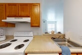 Located at 1645 Rio Hill Dr in Charlottesville, VA, this two-bedroom, two-bathroom residence offers a practical and well-organized single-floor layout. Wood-look flooring runs throughout the entire unit, lending warmth and visual continuity from room to room. The combined kitchen and living area serves as the heart of the home, with the kitchen featuring warm honey-toned cabinetry, ample counter space, and a white electric range with overhead ventilation. The open layout allows for flexible living and dining arrangements. Both bedrooms are comfortably sized, with the primary bedroom offering generous proportions, clean white walls, and a closet with six-panel doors. Natural light enters through blinded windows, and each bedroom benefits from direct access or proximity to a full bathroom. The two bathrooms echo the consistent design language of the space, with wood-toned vanity cabinetry, neutral countertops, and baseboard heating units. A connecting hallway ties the layout together efficiently. The overall aesthetic is clean and neutral, providing a blank canvas adaptable to a variety of interior styles. The unit's single-floor design ensures ease of movement throughout the space.