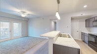 This well-designed 3-bedroom, 2-bathroom single-floor home in Columbus, Ohio offers a comfortable and functional layout. The open-concept kitchen and living area form the heart of the home, featuring a large peninsula with striking marble-look countertops, pendant lighting, and dark-toned cabinetry. Black stainless steel appliances, including a range, microwave, and refrigerator, complement the modern aesthetic. Light wood-style flooring runs through the kitchen and main areas, transitioning to plush carpet in the living room and bedrooms. The living area is accented by a ceiling fan and flows seamlessly from the kitchen. The primary bedroom is generously sized, featuring French doors that bring in natural light, a ceiling fan, and a spacious walk-in closet with wire shelving. Additional bedrooms offer carpet flooring, natural light through windows with exterior views, and closet storage. The bathrooms are finished with wood-look flooring, dark vanity cabinetry, and marble-look countertops. A hallway connects all rooms efficiently, with three closets providing ample storage throughout. The home presents a clean, contemporary palette of neutral tones, creating a bright and inviting atmosphere throughout.