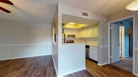 Located at 2481 NE Coachman Rd in Clearwater, Florida, this single-floor residence offers a well-organized and functional layout designed for comfortable everyday living. The open-concept living and dining area is finished with rich, dark hardwood-style flooring that extends throughout the main living spaces, creating a warm and cohesive aesthetic. A textured popcorn ceiling and chair-rail molding add classic architectural character to the interior walls.

The kitchen is positioned as a semi-open pass-through, featuring white cabinetry, a stainless steel stove and dishwasher, a built-in refrigerator, and a raised breakfast bar that connects seamlessly to the dining and living areas. A recessed soffit with warm lighting above the kitchen adds a distinctive design touch.

The living area is bright and airy, anchored by a ceiling fan with a light fixture and a large sliding glass door fitted with vertical blinds that opens to a private balcony, offering views of the surrounding greenery. A pendant light fixture serves as an elegant accent in the dining space.

The bedroom is a quiet retreat, featuring plush carpeting, a large window that invites natural light, and neutral-toned walls. An additional room with hardwood-style flooring and a ceiling fan provides flexible space for a home office or guest room. The unit is served by central HVAC with ceiling vents throughout.