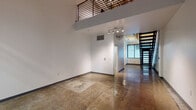 Located at 430 S Broadway in the heart of Downtown Los Angeles, this two-story loft delivers an industrial-modern aesthetic defined by polished concrete floors, crisp white walls, and an open, versatile layout. The main level impresses with soaring double-height ceilings and floor-to-ceiling black-framed glass doors that open directly onto a private outdoor patio, filling the space with natural light and providing seamless indoor-outdoor connectivity. Track lighting and exposed piping add to the loft's urban character throughout. The compact kitchen is efficiently appointed with stainless steel appliances, including a refrigerator, electric range, dishwasher, and microwave, complemented by white cabinetry and a clean countertop. A full bathroom on the main level features a glass-enclosed tiled shower and a floating vanity. A striking staircase with a metal railing connects to the upper level, which overlooks the main floor through an open mezzanine balustrade. The upper floor includes a bedroom with dual closets and exposed ceiling beams, along with a second bathroom featuring a wall-mounted vanity. The space also includes large windows with roller shades, offering urban views of the surrounding Downtown LA streetscape.
