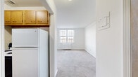 This 2-bedroom, 1-bathroom unit is thoughtfully laid out across a single floor, making efficient use of its compact footprint. The space is organized around a central hallway that connects the kitchen, bedrooms, and bathroom.

The primary bedroom is the most spacious room in the unit, featuring neutral carpet flooring, bright white walls, and a pair of double-hung windows with blinds that frame views of the surrounding neighborhood. A radiator beneath the windows provides heating. The second bedroom is more intimate in scale, also finished with carpet and white walls, offering a clean and versatile space.

The kitchen is fitted with wood-tone cabinetry, granite-patterned countertops, a stainless steel sink, and a tile backsplash. Light wood-style flooring and cream ceramic wall tiles give the kitchen a functional, classic character. A full-size refrigerator and electric range complete the setup.

The bathroom features retro-style cream and black ceramic wall tiles, a white pedestal-style vanity with a mirror, and a full soaking tub with a shower. The tile work adds a distinctive vintage aesthetic to the space.

Throughout the unit, white walls and natural light from multiple windows create a bright, airy ambiance, while carpet flooring in the living areas adds warmth and comfort.