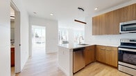 Located at 22 W Camden St in Hackensack, NJ, this single-floor unit showcases a thoughtfully designed, modern interior defined by clean lines, bright white walls, and light hardwood flooring that runs consistently throughout the space.

The open-concept kitchen serves as a central feature, anchored by a large peninsula with a striking veined quartz countertop and an undermount sink. Warm wood-toned cabinetry extends both above and below, complemented by stainless steel appliances, including a range, built-in microwave, and dishwasher. A linear pendant light fixture suspended overhead adds a refined focal point.

The living area benefits from an expansive arrangement of floor-to-ceiling windows, allowing abundant natural light to pour in and offering open views of the surrounding neighborhood. A curved bay window configuration in one room further enhances the sense of brightness and airiness.

The bedroom spaces feature large windows that continue the home's emphasis on natural light, with clean white walls and hardwood floors maintaining a cohesive, minimalist aesthetic.

The bathroom is finished with large-format tile, a glass-enclosed walk-in shower, a wood-accented vanity with a white countertop, and coordinating tile flooring, creating a polished, spa-like atmosphere.