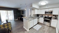 This 2-bedroom, 2-bathroom residence spans a single floor and offers a thoughtfully designed open-concept layout that maximizes space and flow. The kitchen serves as the heart of the home, featuring white shaker-style cabinetry, granite countertops, a peninsula with a double-basin sink, and stainless steel appliances, including an electric range and microwave. Pendant lighting and flush-mount ceiling fixtures provide warm, functional illumination throughout. The kitchen opens seamlessly into the living area, which is accented by a bold slate-gray feature wall and durable wood-look plank flooring that extends throughout the main living spaces, adding warmth and visual continuity. Natural light filters in through sliding glass doors in the living area, enhancing the bright and airy feel of the space. The neutral color palette and clean lines create a modern yet welcoming ambiance, while the open layout offers flexibility for a variety of furnishing arrangements. With two full bathrooms and two generously sized bedrooms, this residence balances comfort and practicality, making it well-suited for a range of lifestyles.