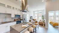This well-appointed 2-bedroom, 2-bathroom residence offers a thoughtfully designed single-floor layout with modern finishes and abundant natural light throughout. The open-concept kitchen is a standout feature, showcasing white shaker cabinetry extending to the ceiling with frosted glass upper panels, granite countertops, a subway tile backsplash, stainless steel appliances, and a central island with bar seating topped by a sleek stainless range hood — ideal for both cooking and entertaining. The kitchen flows seamlessly into the living room, where soaring ceilings and expansive floor-to-ceiling windows frame outdoor views and flood the space with sunlight. Light wood flooring runs throughout, enhancing the bright, airy ambiance. The primary bedroom is a comfortable retreat with large windows offering scenic outdoor views. The second bedroom is equally inviting, benefiting from natural light and ample space. Both bathrooms are finished with granite vanity counters and white cabinetry; one features a tub-shower combination with marble-style tile surround, while the other includes a glass-enclosed walk-in shower. A dedicated closet provides additional storage. The overall design aesthetic is clean, contemporary, and cohesive, making this a refined and functional living space.
