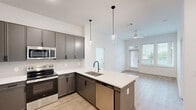 Located in Cornelius, NC, this thoughtfully designed 2-bedroom, 2-bathroom residence offers a clean, contemporary aesthetic throughout. The open-concept kitchen and living area serves as the heart of the home, showcasing a large center island with quartz countertops, an undermount sink with a matte black faucet, and sleek gray cabinetry. Stainless steel appliances, a subway tile backsplash, and modern glass pendant lights complete the kitchen's polished look. Light wood-look flooring flows through the main living areas, which benefit from abundant natural light and direct access to a private balcony through a glass-paneled door. The spacious primary bedroom features plush carpet and a generously sized closet with wire shelving organization systems. The primary bathroom offers a dual-sink vanity with white quartz counters, gray cabinetry, matte black hardware, and a large mirror with contemporary lighting. The second bedroom is bright and airy, with large windows framing outdoor views and soft carpet underfoot. The second bathroom mirrors the modern design language with a single-sink vanity, a tub-shower combination, and consistent matte black fixtures. Two dedicated closets provide ample storage throughout the residence.