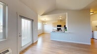 This thoughtfully designed 2-bedroom, 2-bathroom single-floor unit offers a clean, contemporary aesthetic throughout. Light wood-tone vinyl flooring runs continuously across the entire space, creating a cohesive and bright atmosphere. The open-concept kitchen and living area form the heart of the unit, where vaulted ceilings amplify the sense of space. The kitchen features light wood cabinetry with matte black hardware, white quartz countertops, black appliances including a range and microwave, and a peninsula that provides additional counter and prep space. A dedicated dining area sits adjacent to the kitchen, lit by a modern chandelier and a large window overlooking the neighborhood. The living area benefits from a ceiling fan and a sliding glass door that invites natural light and outdoor access. The primary bedroom is a well-proportioned retreat with vaulted ceilings, a ceiling fan, a private door to an outdoor balcony, and access to a walk-in closet. The second bedroom is bright and airy with a large window. Both bathrooms are finished with light wood vanities, white quartz counters, large mirrors, and tub-shower combinations. A dedicated in-unit laundry area with a full-size washer and dryer adds exceptional convenience to this well-appointed home.