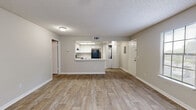Located at 2121 Burwick Ave in Orange Park, Florida, this single-story residence offers a clean, functional layout with consistent light wood-look flooring and neutral warm-gray tones throughout. The open-concept living area is generously sized, featuring a ceiling fan with integrated lighting, a textured ceiling, and large windows fitted with vertical blinds that allow ample natural light. A sliding glass door opens directly to an outdoor area, offering views of surrounding greenery that bring a refreshing sense of nature indoors. The living space connects seamlessly to a well-appointed kitchen, which features a peninsula breakfast bar, white cabinetry, light countertops, a stainless range, and a black refrigerator. A dedicated laundry closet with a stacked washer and dryer is conveniently accessible just off the kitchen. The bedroom is well-proportioned, equipped with a ceiling fan and a sliding glass door providing additional outdoor access and natural light. It includes a walk-in closet, offering practical storage space. The bathroom is neatly finished with a white vanity, a large mirror, and a full tub-shower combination. Throughout the unit, clean white trim, consistent flooring, and a cohesive neutral palette create a bright and welcoming atmosphere.
