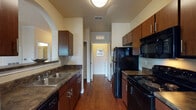 This single-story unit presents a thoughtfully designed layout that balances open communal areas with private living spaces. The entryway corridor, finished with plush carpeting and crown molding, features track lighting overhead and a charming arched pass-through niche, providing a welcoming introduction to the home.

The galley-style kitchen is outfitted with rich dark wood cabinetry, dark granite-style countertops, hardwood flooring, and a full suite of black appliances including a refrigerator, range, microwave, and dishwasher. A double stainless steel sink lines one wall, maximizing workspace efficiency.

The living area is carpeted and accented with crown molding and a ceiling fan. French doors open to an outdoor area, filling the room with natural light and exterior views. A dining nook off the main corridor accommodates a bistro-style table and seating beneath track lighting.

The bedrooms are carpeted and generously sized, each featuring ceiling fans and windows that bring in natural light. The bathroom includes hardwood flooring, a dark wood vanity with a large mirror, and a tub-shower combination. Overall, the unit maintains a warm, neutral palette throughout.