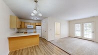 Located at 18 Pavement Rd in Lancaster, NY, this 2-bedroom, 1-bathroom single-floor unit offers a thoughtfully laid-out living space with a clean, neutral aesthetic throughout. The open-concept living area seamlessly connects the kitchen, dining, and living room into one cohesive space. The kitchen is equipped with light maple cabinetry, white appliances including a range, microwave, dishwasher, and refrigerator, and a peninsula with a pendant chandelier overhead that adds a warm focal point to the room. Wood-look plank flooring runs through the kitchen and dining area, while soft carpet extends into the living room and bedrooms. The living room is bright and airy, highlighted by French doors that invite natural light and provide outdoor access. Both bedrooms are carpeted and feature neutral walls with natural light from windows overlooking the surrounding neighborhood. The primary bedroom offers a comfortable, well-proportioned layout. The bathroom is finished with wood-tone cabinetry, a single vanity, a lighted mirror, and a glass-enclosed shower stall with hardwood-style flooring. Four closets are distributed throughout the unit, providing generous storage. The overall ambiance is clean, functional, and move-in ready.