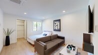 Located at 7810 Topanga Canyon Boulevard in Los Angeles, CA, this thoughtfully designed one-bedroom, two-bathroom unit offers a clean, modern aesthetic across a single floor. The open-concept bedroom and living area features light hardwood flooring, recessed lighting, and crisp white walls that create a bright and airy atmosphere. A window brings in natural light and greenery views, enhancing the welcoming ambiance of the main room. A dedicated closet provides practical storage.

The kitchen is efficiently designed with dark espresso cabinetry, white countertops, and a full suite of stainless steel appliances including a gas range, built-in microwave, dishwasher, and a full-size refrigerator — offering a well-equipped cooking space.

Both bathrooms are finished in a contemporary style, featuring warm wood-toned vanity cabinetry, white quartz countertops, and light wood-look tile flooring. One bathroom includes a tub and shower combination with sliding glass doors, while the other features a clean, minimal layout. Recessed lighting and backlit mirrors add a polished touch throughout. A hallway connects the spaces, completing this cohesive and functional single-level layout.