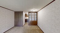 Located at 1173 Spruce Ct in Kent, Ohio, this single-floor unit offers a practical and functional layout across a compact footprint. The main living area is carpeted and features textured walls with neutral tones, dark wood crown molding, and a textured ceiling with flush-mount lighting. A prominent dark wood built-in shelving and cabinet unit serves as a natural room divider, offering both open display shelving with arched details and closed lower cabinet storage — a distinctive architectural feature of the space.

The entry wall features a white front door flanked by a large window dressed with vertical blinds, allowing natural light to filter into the living area. A wall-mounted HVAC unit provides climate control beneath the window. Adjacent to the main living space, a kitchenette area is visible, outfitted with dark wood cabinetry and a sink, providing essential cooking and prep functionality. A full-panel closet with sliding doors adds generous storage to the living area.

The bathroom is clean and well-appointed, featuring light marbled wall panels, tile flooring, a toilet, and a vanity with a granite-style countertop and undermount sink, complemented by chrome towel bar fixtures and a wall mirror. The overall design reflects a classic, utilitarian aesthetic well-suited for efficient single-occupant living.