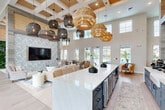 Located at 345 Burbank Ave in Ponte Vedra Beach, Florida, this thoughtfully designed single-floor clubhouse space offers a generous and versatile layout ideal for community living. The open-concept floor plan seamlessly connects a stylish living area and dining space, unified by wide-plank light wood flooring that flows throughout.

The living room serves as the centerpiece, boasting soaring double-height ceilings, a dramatic accent wall featuring a botanical-print wallcovering framing a mounted flat-screen display, and an eye-catching cluster of woven pendant lights. Large windows and glass entry doors flood the space with abundant natural light while offering views of the outdoor pool area and surrounding landscape.

The dining area features built-in bench seating with marble-topped tables, accented by elegant woven pendant lighting and coastal-themed wall art, creating a warm and inviting atmosphere reflective of the Ponte Vedra Beach locale.

A dedicated workspace or conference area includes a tray ceiling painted in soft blue-gray, adorned with ornate gold chandeliers, a long white conference table with ergonomic seating, a wall-mounted display, and frosted glass-paneled doors for privacy. A living green wall adds a vibrant natural element near the main gathering area, tying the coastal and organic design themes together cohesively throughout the space.