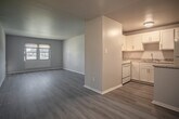 Located at 611 Michigan Dr in Hampton, Virginia, this single-floor unit offers a clean, functional layout with thoughtfully updated finishes throughout. The living area greets you at the entry with durable wood-look plank flooring in a cool gray tone, neutral painted walls, and a window fitted with blinds that allows natural light to filter in from outside. The space flows naturally toward the kitchen, which features white shaker-style cabinetry, granite-look countertops, white appliances including a refrigerator and range, and a peninsula counter with additional storage — ideal for casual dining or meal prep. An adjacent dining or flex area mirrors the same plank flooring and offers a versatile open space. The bedrooms are carpeted in a soft blue-gray tone, each equipped with a closet and windows providing natural light and outdoor views. The bathroom includes a full soaking tub with a white surround panel enclosure, built-in shelving niches, and a vanity with cabinet storage. Throughout the unit, consistent neutral gray tones, white trim, and ceiling-mounted light fixtures create a cohesive and move-in-ready aesthetic suited for comfortable everyday living.
