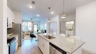 This thoughtfully designed single-floor residence offers a bright, open-concept layout that seamlessly connects the kitchen, dining, and living areas. The kitchen is a standout feature, anchored by a generous granite-topped island with an undermount sink, bar seating, and stylish pendant lighting. White shaker cabinetry, stainless steel appliances — including a refrigerator, range, microwave, and dishwasher — and light wood-style flooring complete the space with a clean, contemporary aesthetic.

The living area is warmly lit by natural light from large windows and features a bold accent wall that adds character and depth to the open floor plan. A ceiling fan overhead enhances comfort throughout.

The primary bedroom is a peaceful retreat, carpeted for comfort, with large windows that invite natural light and a soft blue accent wall. It connects directly to an en-suite bathroom featuring a dual-sink granite vanity, white cabinetry, and wood-look tile flooring. A spacious walk-in closet with multi-level wire shelving provides generous storage.

A dining area adjacent to the kitchen offers dedicated space for meals, and the overall palette of whites and soft neutrals gives the entire residence a fresh, cohesive feel.