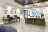 Located in Acworth, Georgia, this single-story community clubhouse at Stanton Place offers a thoughtfully designed gathering space that blends functionality with contemporary style. The main entry opens into a bright, airy reception and leasing area distinguished by soaring vaulted ceilings, large windows dressed with teal drapery, and large-format tile flooring laid in a herringbone-inspired pattern throughout. Natural light pours in through multiple windows, creating an inviting and open atmosphere.

The expansive lounge and common area serves as the heart of the clubhouse, featuring a coffered ceiling section with a dramatic dark wood finish, pendant lighting fixtures, and a mounted flat-screen television. Comfortable seating arrangements — including armchairs, sofas, and accent rugs — provide residents with versatile spaces to relax or socialize. Vibrant abstract artwork adorns the walls, adding a bold, creative character to the interior.

A dedicated business center offers dual workstations equipped with computers and a printer, complemented by a trio of framed abstract art pieces above. A bar-height communal table positioned beside large sliding glass doors frames a picturesque view of the outdoor pool and lush surrounding greenery, seamlessly connecting the interior to the resort-style amenities just beyond.