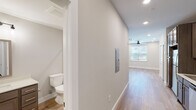 This single-floor unit in Huntsville, Alabama offers a clean, modern interior defined by light wood-look flooring, neutral gray-toned walls, and recessed lighting that runs consistently throughout the space. The layout connects key living areas through a straightforward, well-proportioned corridor that also houses an electrical panel access panel along the wall.

The kitchen is equipped with dark-toned cabinetry featuring sleek bar-pull hardware, stainless steel appliances including a refrigerator, range, microwave, and dishwasher, and a single-basin sink with a light countertop surface. A dedicated laundry closet adjacent to the kitchen area conceals a stacked washer and dryer unit, adding everyday convenience without consuming additional living space.

The main living area is open and airy, featuring a ceiling fan with recessed lighting overhead and a window dressed with horizontal blinds that allows natural light to filter in. The bathroom presents a cohesive, understated design with a wood-toned vanity, light countertop, a tub-shower combination with built-in shelving, and chrome fixtures. Overall, the space maintains a consistent modern aesthetic with practical, well-integrated features suited for comfortable daily living.