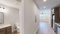 This single-floor unit in Huntsville, Alabama offers a clean, modern interior defined by light wood-look flooring, neutral gray-toned walls, and recessed lighting that runs consistently throughout the space. The layout connects key living areas through a straightforward, well-proportioned corridor that also houses an electrical panel access panel along the wall.

The kitchen is equipped with dark-toned cabinetry featuring sleek bar-pull hardware, stainless steel appliances including a refrigerator, range, microwave, and dishwasher, and a single-basin sink with a light countertop surface. A dedicated laundry closet adjacent to the kitchen area conceals a stacked washer and dryer unit, adding everyday convenience without consuming additional living space.

The main living area is open and airy, featuring a ceiling fan with recessed lighting overhead and a window dressed with horizontal blinds that allows natural light to filter in. The bathroom presents a cohesive, understated design with a wood-toned vanity, light countertop, a tub-shower combination with built-in shelving, and chrome fixtures. Overall, the space maintains a consistent modern aesthetic with practical, well-integrated features suited for comfortable daily living.