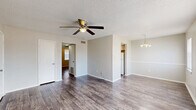 Located at 4001 S 16th St in Fort Smith, Arkansas, this single-story, 3-bedroom, 1-bathroom home offers a straightforward and functional layout across one floor. The living room serves as a welcoming entry point, featuring wood-style plank flooring, a ceiling fan with light fixture, a textured ceiling, and dual front-facing windows that fill the space with natural light. An elegant chandelier accents the adjacent dining area, which connects seamlessly to the kitchen. The kitchen is equipped with white cabinetry, laminate countertops, a range with overhead ventilation hood, and matching wood-style flooring. A central hallway connects the living areas to the three bedrooms and the shared bathroom. Each bedroom features the same durable wood-style flooring, neutral painted walls, textured ceilings, and ceiling fans. Select bedrooms include windows with blinds for natural light and privacy, as well as closets for storage. The shared bathroom includes a tiled tub-and-shower combination with warm-toned mosaic tile surround, a toilet, and a vanity with sink. Throughout the home, consistent finishes and neutral tones create a clean, cohesive atmosphere.