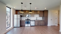 Located at 500 W Broad St in Columbus, Ohio, this modern single-floor residence offers a thoughtfully designed layout with contemporary finishes throughout. The open kitchen is a standout feature, equipped with stainless steel appliances including a refrigerator, electric range, built-in microwave, and dishwasher. Warm-toned flat-panel cabinetry pairs with a white subway tile backsplash and neutral countertops, while industrial-style pendant lights add character overhead. Durable wood-look flooring runs throughout the main living areas, adding warmth and continuity. The living space is exceptionally bright, featuring floor-to-ceiling sliding glass doors that open to a private balcony, alongside large picture windows that frame sweeping views of the Columbus skyline and surrounding neighborhood. The bedroom is carpeted for comfort and also benefits from direct balcony access via a sliding glass door. The bathroom is finished with a white tile walk-in shower enclosed by a glass door with matte black hardware, a wood-toned vanity, and large-format tile flooring. A spacious walk-in closet adjacent to the bathroom provides ample storage. Recessed lighting throughout ensures a clean, polished aesthetic in every room.