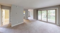 This single-floor residence offers a practical and comfortable layout with a variety of functional spaces thoughtfully arranged throughout. The kitchen is designed for efficiency, featuring light wood cabinetry, dark granite-style countertops, a stainless steel sink, a black electric range, a built-in microwave, and a dishwasher. Light tile flooring and a window overlooking lush greenery give the kitchen a bright, airy feel. Baseboard heating is present throughout the unit, ensuring comfort year-round. The living area is generously proportioned, finished with neutral-toned carpeting and soft gray walls. A sliding glass door opens to a private balcony, flooding the space with natural light and offering views of the surrounding trees. A ceiling fan adds to the room's comfort, and the open sightline to the kitchen creates a cohesive flow. The bedrooms are carpeted and serene, each benefiting from natural light through windows framing wooded views. One bedroom includes a wall-mounted air conditioning unit for added climate control. The bathroom features floor-to-ceiling tile work in warm beige tones, a soaking tub, built-in corner shelving, and a frosted window for privacy. Overall, the space presents a clean, neutral palette with practical finishes throughout.