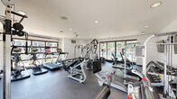 Located at 13820 South 44th Street in Phoenix, AZ, this fitness center offers a dedicated exercise room designed to support a full range of workout routines. The space is housed on a single floor and is laid out to maximize functionality and ease of movement between equipment.

The interior features clean white walls, recessed ceiling lighting, and durable dark rubberized flooring that is both practical and visually cohesive. Large floor-to-ceiling windows and expansive glass panels along one wall flood the room with abundant natural light and provide open views of the surrounding outdoor greenery and pool area, creating an energizing atmosphere.

The exercise room is comprehensively outfitted with multiple treadmills, elliptical machines, and stationary bikes for cardiovascular training, as well as a multi-station cable and weight machine for strength work. A dedicated free weights section includes a full dumbbell rack with an adjustable workout bench nearby. A wall-mounted flat-screen television adds convenience for entertainment during workouts.

The room also features a glass-paned entry door, an emergency exit sign, and proper ventilation systems. The overall ambiance is clean, modern, and well-maintained, making this fitness center a practical and inviting space for daily exercise.