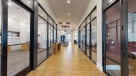 Located at 485 Crafton Cir in Charlottesville, VA, this thoughtfully designed single-floor community space spans a generous footprint, offering a variety of distinct areas for socializing, relaxing, and gathering. The entrance corridor sets an immediate tone of modern sophistication, lined with sleek, dark-framed glass partitions flanking a warm hardwood floor that guides visitors through the space. The grand lobby beyond features soaring tray ceilings, an array of sculptural wall sconces, and abundant recessed lighting, all anchored by large glass doors that draw in natural light and outdoor views. A lounge area offers comfortable, stylishly curated seating with high ceilings and large windows providing views of the surrounding neighborhood. A standout multi-purpose room showcases dramatic floor-to-ceiling brick-framed windows on two walls, flooding the space with natural light and featuring a built-in cushioned window seat for a cozy nook alongside a dining table. The kitchen area is well-appointed with gray shaker cabinetry, patterned tile flooring, stainless steel appliances, a decorative tile backsplash, and striking geometric pendant lighting. A social lounge rounds out the space with high-top tables, a pool table, a dark shiplap accent wall, pendant lighting, and multiple wall-mounted displays, creating an inviting hub for casual interaction.