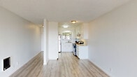 Located at 2100 Miramonte Ave in San Leandro, CA, this single-story one-bedroom, one-bathroom unit offers a well-organized layout across a comfortable floor plan. The kitchen is a standout feature, showcasing crisp white cabinetry with brushed chrome hardware, light wood-look vinyl flooring, white quartz-style countertops, and stainless steel appliances including a refrigerator and range with overhead exhaust hood. A window above the sink brings in natural light, enhancing the clean, modern aesthetic. The combined kitchen and living area provides a versatile open space, with the living room featuring the same light vinyl flooring and a textured ceiling, giving it a bright and airy feel. Vertical blinds lead to what appears to be an outdoor access point, adding connectivity to the exterior. The bedroom is carpeted and features a wide window with views of lush greenery and palm trees, a baseboard heater, and a full-width sliding-door closet offering ample storage. The bathroom is finished in a crisp, all-white palette with subway tile surrounding the bathtub and shower, wood-look flooring, a white vanity with sink, and a clean, functional layout. A hallway connects the rooms efficiently. Overall, the unit presents a fresh, neutral aesthetic throughout.