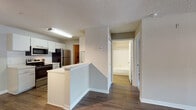 Located at 8801 Hunters Lake Dr in Tampa, Florida, this single-story residence offers a well-organized, functional layout with clean, modern finishes throughout. The open-concept kitchen is a central highlight, featuring stainless steel appliances including a refrigerator, electric range, and over-the-range microwave, complemented by white cabinetry, light stone-style countertops, and a peninsula that provides additional prep space and separates the kitchen from the adjacent living area. The kitchen connects seamlessly to a utility area with additional storage access. The living room is generously proportioned, bathed in natural light from a large multi-pane window, and features warm hardwood-style flooring, a ceiling fan, and built-in wall shelving that adds both character and practicality. Track lighting enhances the open dining and living areas. The bedroom is carpeted for comfort and includes a ceiling fan, ample wall space, and direct access to a walk-in closet area. The bathroom is cleanly appointed with a single-sink vanity featuring a speckled countertop, mirrored medicine cabinet, and a tiled shower-tub combination. Consistent hardwood-style flooring runs through the main living spaces, creating a cohesive and contemporary aesthetic throughout this well-maintained Tampa home.