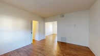 This single-floor residence offers a clean, functional layout with warm hardwood flooring that flows consistently through the living areas, bedrooms, and connecting spaces. The living area is open and well-proportioned, featuring neutral walls, a ceiling vent for climate control, and a wall-mounted heating unit, creating a comfortable and adaptable space. A wide doorway connects the living area to an adjoining room, promoting an open feel throughout the home.

The bedrooms are bright and airy, benefiting from multiple windows fitted with blinds that allow for natural light control. One bedroom includes a ceiling fan with integrated light fixture, along with access to a generous walk-in closet equipped with built-in shelving and a clothing rod, offering ample storage. An additional closet is also accessible from the bedroom corridor.

The kitchen is efficiently designed with white cabinetry, a gas range and oven, a full-size refrigerator, and a door that leads to the exterior — ideal for convenient access. The countertops provide practical workspace, and the layout supports ease of movement.

The bathroom features a full tub-shower combination with white tile surround, accented by a classic dark tile border, complemented by a window that brings in natural light. Throughout the home, the consistent use of light, neutral tones and hardwood flooring creates a cohesive and inviting atmosphere.