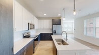 This single-floor unit showcases a thoughtfully designed, contemporary interior with a cohesive neutral palette and modern finishes throughout. The kitchen serves as a standout feature, combining white upper cabinetry with dark wood-toned lower cabinets and a clean white quartz countertop. A central island with an undermount sink and globe pendant lighting adds both functionality and style. Stainless steel appliances, including a French door refrigerator, electric range, and built-in microwave, complete the space. Light wood-style flooring runs through the kitchen and connects seamlessly to an adjacent living area filled with natural light from multiple windows.

The bedrooms feature plush carpeting and large windows with blinds that allow ample natural light. At least one bedroom includes a walk-in closet with built-in shelving, providing generous storage. White panel doors with matte black hardware appear consistently throughout, adding a modern farmhouse touch.

Two bathrooms serve the unit: one featuring a sliding glass-door walk-in shower with chrome fixtures, and another with a full soaking tub and shower combination. Both bathrooms feature light wood-style flooring and clean white finishes, maintaining the unit's bright, modern aesthetic.