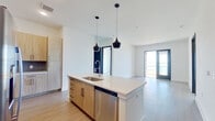This well-designed 2-bedroom, 3-bathroom single-floor residence offers a thoughtful open-concept layout with clean, contemporary finishes throughout. The kitchen serves as a central hub of the living space, featuring light wood cabinetry, a striking blue herringbone tile backsplash, stainless steel appliances, a built-in wine rack, and a large island with a white quartz countertop, undermount sink, and pendant lighting overhead. The kitchen flows seamlessly into the living area, which is bathed in natural light and opens to a private balcony through full-length glass doors revealing sweeping waterfront views. Both bedrooms are carpeted and generously sized, with the primary bedroom offering dual windows that frame stunning panoramic water views and a ceiling fan. A dedicated closet provides ample storage. The bathrooms are finished with wood-look tile flooring and warm cabinetry, with one bathroom featuring a soaking tub and shower combination. Black-framed interior doors add a bold, modern contrast against the crisp white walls, while light wood-style flooring ties together the main living areas. The overall ambiance is bright, clean, and contemporary, with the waterfront scenery serving as a defining and breathtaking feature throughout the space.