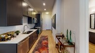 Located at 2100 South Blvd in Charlotte's vibrant Dilworth neighborhood, this single-floor residence offers a thoughtfully designed open layout with contemporary finishes throughout. Light wood-tone flooring flows seamlessly across the entire space, creating a warm and cohesive aesthetic.

The galley-style kitchen is outfitted with dark cabinetry, white quartz countertops, a subway tile backsplash, and stainless steel appliances, including a refrigerator, microwave, and range. A stainless steel undermount sink completes the functional yet stylish workspace.

The living area is defined by a bold teal accent wall that visually separates it from the sleeping space, adding depth and character. Multiple windows allow natural light to fill the room, while a door provides direct access to an outdoor area. The open-concept arrangement makes the space feel airy and versatile.

The bathroom features warm wood-tone flooring, a dark-framed vanity with a white sink, a large mirror, and a tiled shower surround. An adjacent walk-in closet with built-in shelving provides generous storage.

Overall, this residence blends modern design with practical functionality, offering a comfortable and stylish living environment in one of Charlotte's most sought-after urban neighborhoods.