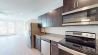This single-floor unit offers a thoughtfully designed layout with modern finishes and functional spaces. The kitchen is a standout feature, showcasing dark espresso-toned cabinetry with sleek bar-pull hardware, neutral-toned countertops, and a full suite of stainless steel appliances, including an electric range, over-the-range microwave, dishwasher, and refrigerator. A gold-accented faucet adds a contemporary touch to the undermount sink. Light wood-look flooring runs throughout, lending warmth and visual continuity across the space.

A hallway with a sliding barn door connects the kitchen area to the rest of the unit, adding a stylish architectural detail. The living area is bright and open, benefiting from natural light streaming through multiple windows fitted with white blinds, as well as French doors that lead to an outdoor area. A ceiling fan overhead enhances comfort in this airy space.

The bathroom features clean, neutral finishes with a dark-toned vanity and gray countertop, complemented by a brushed nickel towel bar. Conveniently adjacent is a dedicated laundry nook housing a stacked washer and dryer unit, adding everyday practicality to the space.