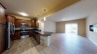 Located at 1 Palms Court in Carlisle, Pennsylvania, this single-floor residence offers a thoughtfully designed open-concept layout that seamlessly connects the kitchen and living areas. The kitchen is a standout feature, showcasing rich cherry-toned cabinetry, dark granite countertops, and a full suite of stainless steel appliances, including a refrigerator, range, microwave, and dishwasher. A curved breakfast bar with a stacked stone base adds a distinctive architectural detail, while pendant lighting overhead enhances the warm, inviting atmosphere. The kitchen floor features large-format stone-look tile, transitioning smoothly into the light hardwood-style flooring of the open living area.

The living space is bright and comfortable, benefiting from a sliding glass door that brings in natural light and provides outdoor access. A sleek wall-mounted electric fireplace serves as a modern focal point on the opposite wall. A hallway leads to the bedrooms, which feature plush carpeting and windows with outdoor views. The bathrooms are finished with large-format tile flooring and include a glass-enclosed tub/shower combination with tile surround. A generously sized walk-in closet with wire shelving and carpeted flooring provides ample storage throughout this well-finished residence.
