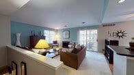 This single-floor residence offers a thoughtfully designed layout with a variety of well-defined living spaces. The living room serves as the centerpiece, featuring soft blue-painted walls, plush carpeting, and a tiled fireplace flanked by armchairs. Natural light fills the room through multiple windows and a large sliding glass door that opens to an outdoor deck, providing views of surrounding trees. A substantial wooden cabinet and layered lighting add warmth and functionality to the space.

The kitchen is open and practical, featuring a peninsula with dark countertops, light wood cabinetry, and stainless steel appliances. It connects directly to the dining area, which includes hardwood flooring, a ceiling fan, and windows that bring in additional natural light. A dedicated dining nook accommodates a glass-top table with seating for four.

The bedroom is spacious and tranquil, dressed in muted blue-green tones with soft carpeting. A secondary room functions flexibly as a sitting or guest room, featuring neutral walls and a daybed. The full bathroom is finished with tile flooring, a tub-shower combination with checkered tile accents, a vanity with ample storage, and blue walls that tie back to the home's unified color scheme throughout.