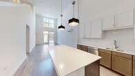 Located in Chicago's vibrant Ravenswood neighborhood, this two-story home offers a thoughtfully designed layout spread across two levels. The main floor commands attention with dramatic double-height ceilings that flood the open-concept living and kitchen area with natural light. Oversized windows and glass doors frame views of the tree-lined street, reinforcing the bright, airy atmosphere throughout. Light wood flooring runs seamlessly across the space, complementing the clean white walls.

The modern kitchen is a standout feature, centered around a large island with a crisp white quartz countertop and contrasting dark wood cabinetry below. Stainless steel appliances, white upper cabinets with subway tile backsplash, and industrial-style pendant lights complete the chef-ready space. The kitchen flows naturally into the living area, making it ideal for entertaining.

Upstairs, the second level houses the primary bedroom suite and an additional bedroom, each benefiting from natural light and closet space. Three well-appointed bathrooms are distributed across both floors, including one with a glass-enclosed walk-in shower. A dedicated utility room with a full-size washer and dryer adds everyday convenience, while a loft provides flexible bonus space. Light wood flooring and a consistent neutral palette create a cohesive, modern feel throughout.