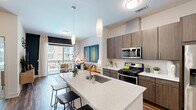 This thoughtfully designed one-bedroom, one-bathroom residence offers a contemporary open-concept layout that maximizes its comfortable footprint. The kitchen serves as a central showpiece, featuring sleek quartz countertops, a large waterfall island with an undermount sink and bar seating, rich wood-tone cabinetry, a subway tile backsplash, stainless steel appliances including a gas range, built-in microwave, and French door refrigerator, all illuminated by modern pendant lighting and warm wood-look flooring. The kitchen flows seamlessly into the living area, which is bathed in natural light from floor-to-ceiling sliding glass doors that open onto a private balcony with outdoor views. The bedroom offers plush carpeting, multiple windows for abundant natural light, a dedicated closet, and ample space for a full furniture arrangement. The bathroom is well-appointed with large-format tile flooring, a wood-tone vanity with quartz countertop, a full soaking tub with shower, and a bold accent wall. Throughout the residence, clean architectural lines, neutral tones, and modern fixtures create a cohesive and polished ambiance.