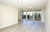 This single-floor residence offers a thoughtfully designed layout with a clean, modern aesthetic throughout. The expansive living area is finished with smooth hardwood-style flooring and warm neutral-toned walls, creating a bright and welcoming atmosphere. Large sliding glass doors line one side of the living space, flooding the room with natural light and providing direct access to a private outdoor patio area with surrounding greenery — a standout feature that seamlessly connects indoor and outdoor living.

The galley-style kitchen is efficiently arranged with warm oak cabinetry on both sides, granite-look countertops, and a full suite of black appliances including a refrigerator, electric range with over-the-range microwave, and a double sink. The layout maximizes counter and storage space, making it highly functional for everyday use.

The bedroom features plush carpeting and a built-in closet equipped with shelving and a hanging rod, offering generous and organized storage. The full bathroom is well-appointed with wood-look vinyl flooring, a white vanity with sink, a tiled shower-tub combination with decorative accent tiles, and chrome grab bars and fixtures for added convenience. Together, these spaces create a comfortable, practical, and inviting home.