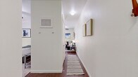 Located in Austin, TX, this efficiently designed one-bedroom, two-bathroom studio makes excellent use of its compact footprint. A welcoming hallway with clean white walls and dark hardwood-style flooring leads into the main living area, setting a modern, understated tone throughout.

The kitchen is a standout feature, offering rich dark wood cabinetry, light countertops, stainless steel appliances including a microwave and dishwasher, a black range, and a peninsula with bar seating. A glass door adjacent to the kitchen provides natural light and outdoor access, enhancing the sense of openness.

The bedroom is a cozy, well-defined retreat with neutral walls, hardwood-style floors, and thoughtful wall art, providing a calm and comfortable atmosphere. A dedicated nook serves as a functional home office space, complete with room for a full desk setup — a practical feature for remote work or study.

Two bathrooms serve the unit, one featuring a tub-shower combination with classic white tile. An in-unit laundry area with shelving adds everyday convenience. Throughout the space, consistent flooring, neutral tones, and clean lines create a cohesive, modern aesthetic well-suited to Austin's vibrant urban lifestyle.