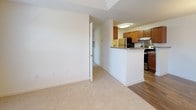 This single-floor residence offers a thoughtfully designed layout with a clear distinction between living and private spaces. The kitchen is equipped with warm wood cabinetry, granite-style countertops, and black stainless appliances including a range and refrigerator. A peninsula counter separates the kitchen from the adjoining dining area, which features rich hardwood-style flooring and an elegant chandelier overhead.

The living areas transition seamlessly between hardwood-style and plush carpeted flooring. Multiple bedrooms are present, each carpeted for comfort and filled with natural light from large windows overlooking lush greenery. One bedroom features a tray ceiling with a ceiling fan, adding an architectural detail that enhances the sense of space. Closet storage is included in the bedrooms, with one showcasing a convenient reach-in closet.

The bathroom is fitted with a full tub-shower combination, a granite-topped vanity, and clean, neutral finishes throughout. A dedicated laundry area houses a side-by-side Whirlpool top-load washer and dryer, offering the convenience of in-unit laundry. Wire shelving provides additional storage in the laundry space. Overall, the residence presents a clean, move-in-ready aesthetic with consistent neutral tones and practical finishes throughout.